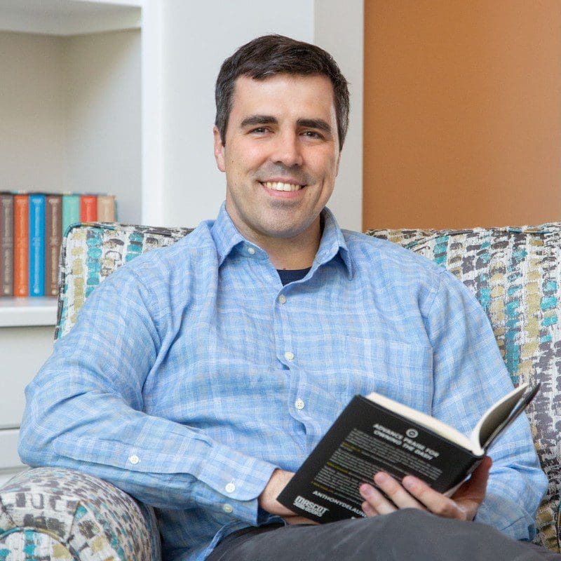 A man sitting on top of a couch holding an open book.